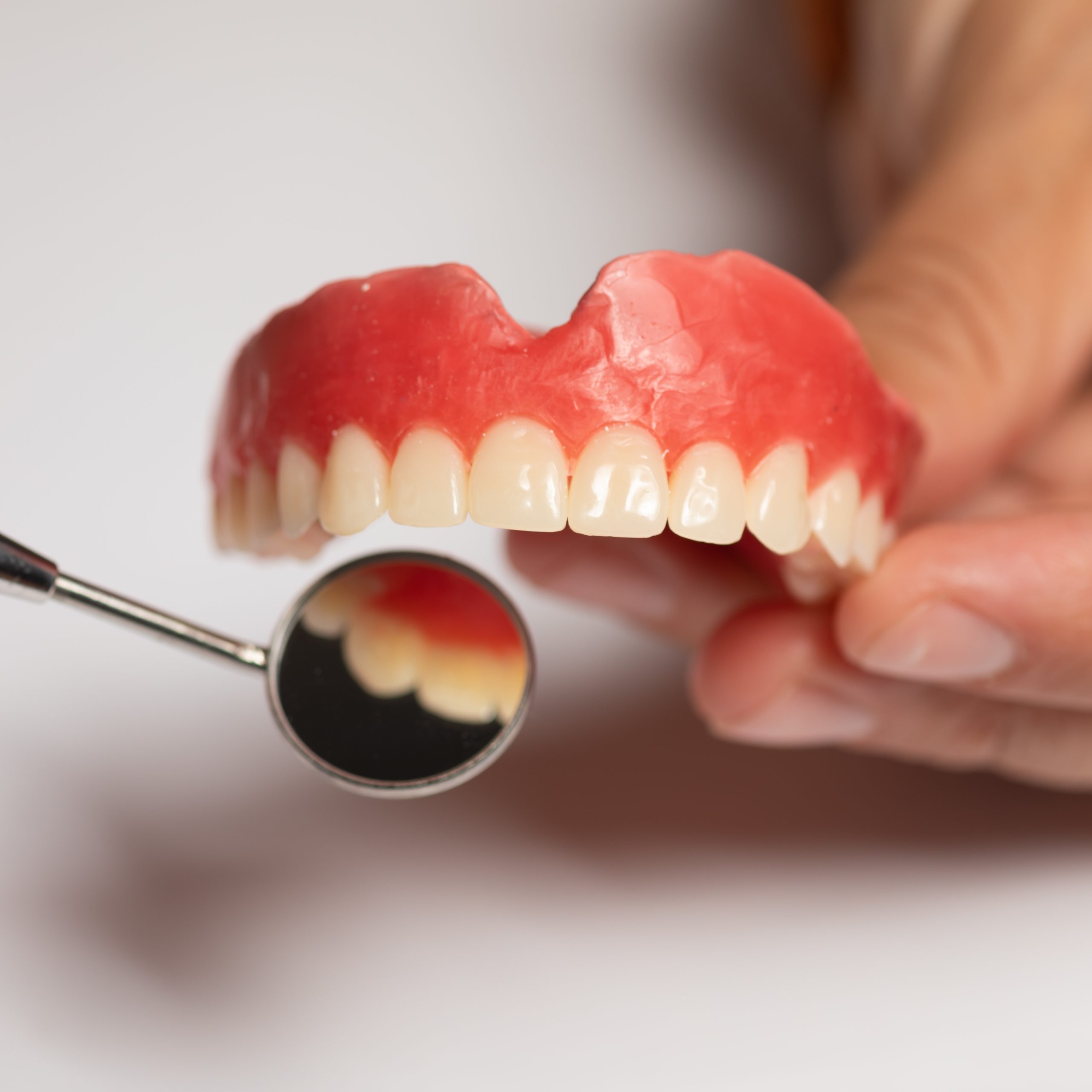 Denture prosthesis in doctor dentist hands, checking with mirror